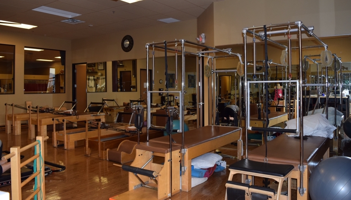 Warm studio interior with wooden reformer exercise machines, mirrors, and polished wood flooring